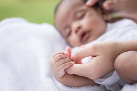 Close up baby's hand holding her mother's hand on the white cloth mattress in the lawnの写真素材