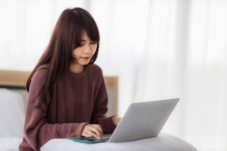 Asian woman using laptop for working, educational, e-commerce, social media in her bed. corovavirus covid-19, stay at home, work form home concept.の写真素材