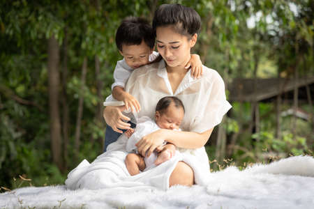 Beautiful Asian young mother  or single mom with new born baby girl and son are doing activities and relaxing in the park. concept of duties of wife and mother in raising children and family.の写真素材