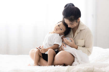 Young Asian mother hugging a cute newborn baby and feeding milk form bottle in with the son white bedroom. Duty of the wife to raise children. Mother and child conceptの写真素材