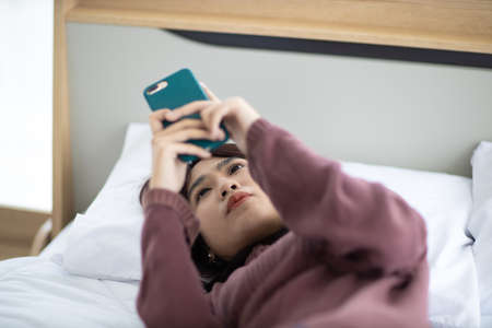 Asian woman watching media from phone in a bedroom in her bedroom feeling lonely. The concept of...
