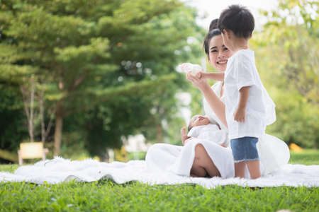 Beautiful Asian young mother  or single mom with new born baby girl and son are doing activities and relaxing in the park. concept of duties of wife and mother in raising children and family.の写真素材
