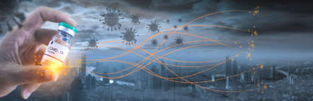 hand holding a COVID-19 vaccine against the background of a city where the coronavirus is spreading. COVID-19 virus protection and vaccine invention and production concept.の写真素材