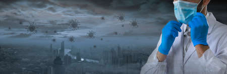 Young doctor wearing rubber gloves is wearing a mask against the background of a large city that resembles an abandoned city spread by coronavirus. Medical vaccine and hope concept.の写真素材
