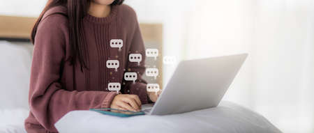 Woman using laptop in bed in bedroom for social network chat with chat box icons. concept of using the Internet in social networks and work from home.の写真素材
