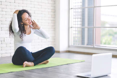 Beautiful young latin woman slim woman live streaming training or learning yoga with laptop in bedroom. Stay at home and self-quarantine in spread of coronavirus covid-19の写真素材