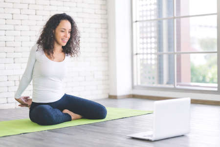 Beautiful young latin woman slim woman live streaming training or learning yoga with laptop in bedroom. Stay at home and self-quarantine in spread of coronavirus covid-19の写真素材