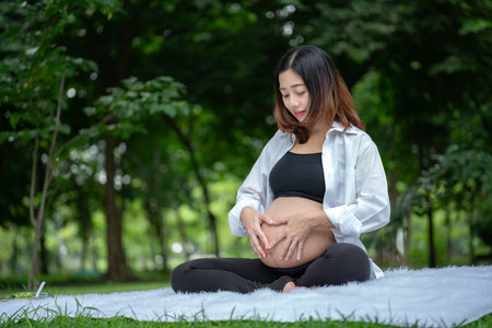 Portrait of Asian pregnant woman relaxing and posing with heart shaped hands on belly in parkの写真素材