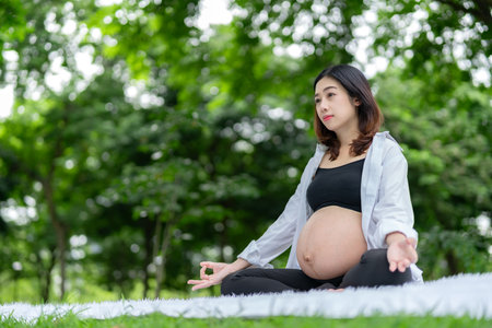 Portrait of asian pregnant woman relaxing by meditating in parkの写真素材