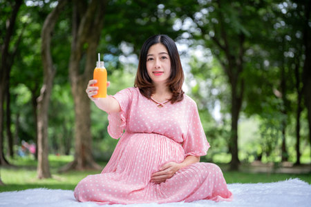 Portrait of Asian pregnant woman relaxing and drinking orange juice in the parkの写真素材