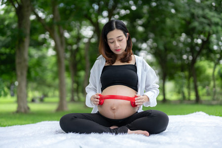 Portrait of Asian pregnant woman relaxing and in the park. Young woman uses headphones on her stomach to let her fetus listen to music.の写真素材