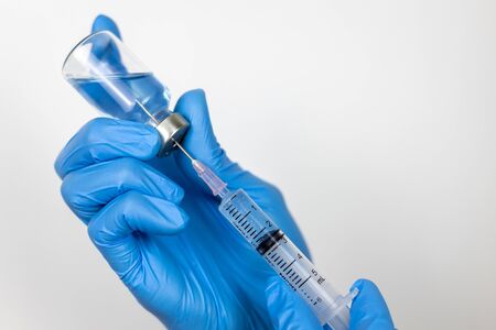 Healthcare concept with a hand in blue medical gloves holding Coronavirus vaccine in syringe.