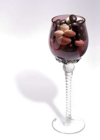 Violet wineglass with tasty chocolate sweets on white backgroundの写真素材