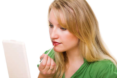 Young woman looking into mirror and putting on lipstick  against white backgroundの写真素材
