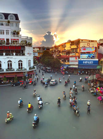 A very busy junction in Hanoi Vietnam with lots of motorbikes and car traffic at sunset. の素材