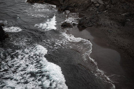 Black sand beach aerial view. Small volcanic rocks and graphic diagonal wavesの写真素材