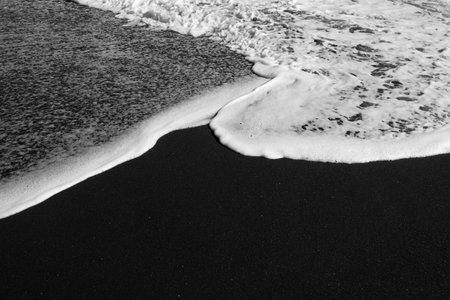 Mostly blurred black sand beach with white foam of sea waves backgroundの写真素材