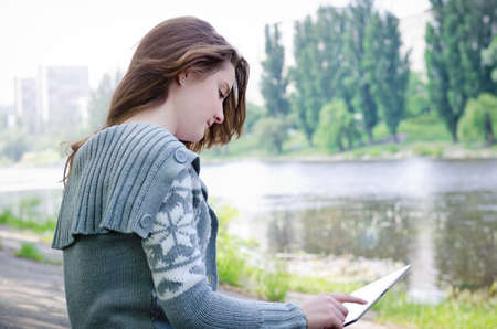 Girl sitting outdoors on a paved driveway in a riverbank using a touchscreen tablet