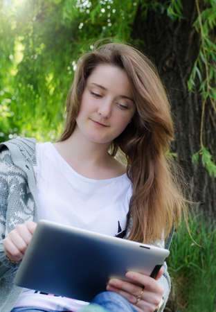 Low angle view of an attractive casual young girl working on a touch screen tablet in the parkの写真素材