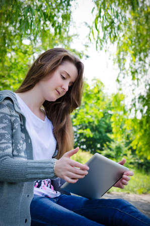 Girl sitting outdoors on a paved driveway in a verdant garden using a touchscreen tabletの写真素材