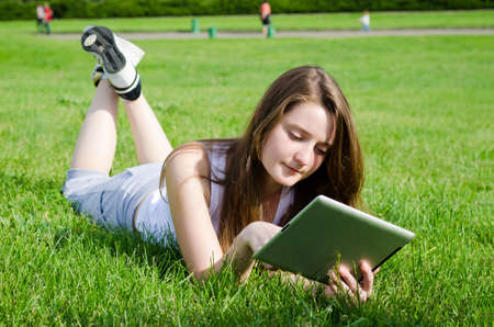Young woman or student lying on her stomach in the green grass using a tablet notebookの写真素材