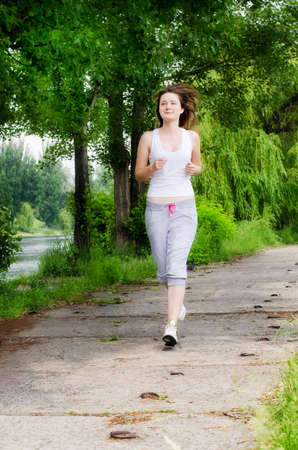 Girl  jogging along a path through a park as she takes her daily exercise to keep fitの写真素材