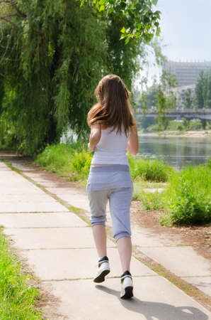 Young woman jogging away from the camera along a pathway running alongside a river in a health and fitness conceptの写真素材