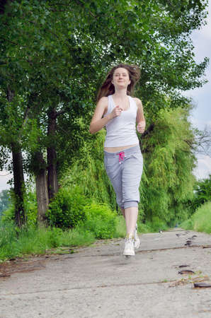 Young woman in casual clothes jogging along a path through a park as she takes her daily exercise to keep fitの写真素材