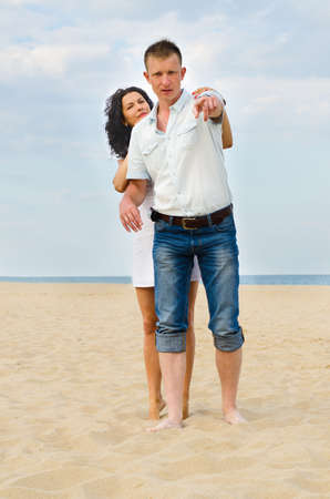Attractive young couple on a beach with the man pointing out something to his wife who is hugging him from behindの写真素材