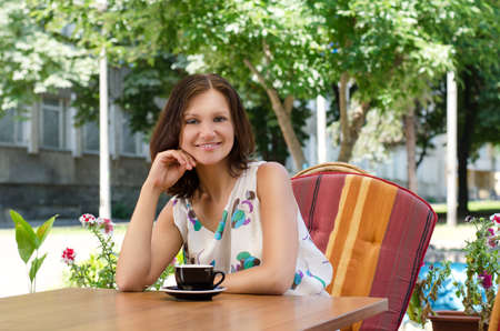 Happy woman seated in a comfortable chair at a table at an outdoor restaurant enjoying a cup of coffeeの写真素材