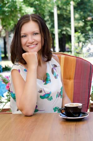 Attractive woman drinking a cup of cappucino coffee seated outdoors at a table in her gardenの写真素材