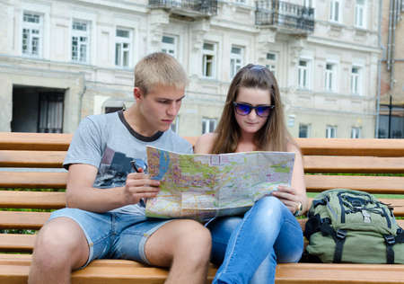 Young tourists sitting on a wooden bench in an urban environment looking at a mapの写真素材