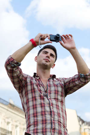 Low angle view of a young man taking a photograph with a compact camera against a cloudy blue sky