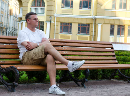 Casual middle-aged man sitting waiting on a wooden bench in an urban environmentの写真素材
