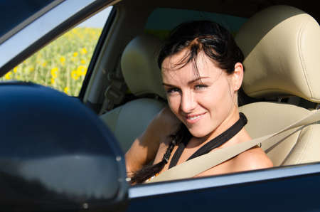 Beautiful smiling young woman wearing a seatbelt seated in a motor car looking out of the window