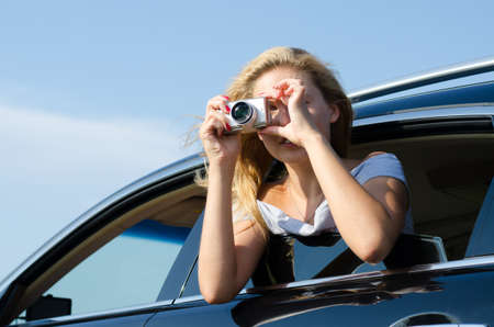 Woman photographer leaning out of car window taking a photo with a compact digital cameraの写真素材
