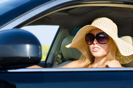 Woman driver in sunhat and sunglasses looking out through the open car window