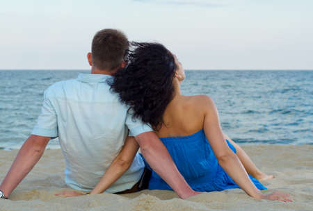 Rear view of a romantic couple sitting in the sand on a tropical beach admiring the oceanの写真素材