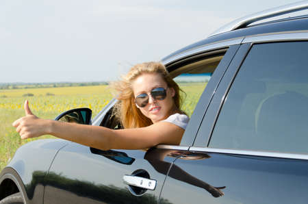Attractive blonde woman leaning out of a car car giving a thumbs up either to show that everything...