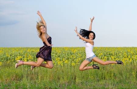 Acrobatic women leaping in unison with their legs high and arms outstretched alongside a field of sunflowersの写真素材