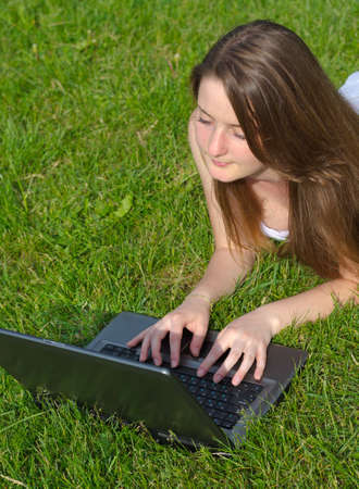 High angle view of an attractive young woman using a laptop while lying on her stomach in green grassの写真素材