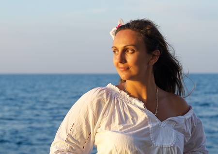 Beautiful woman with a flower in her hair standing with her back to the sea in golden evening light...