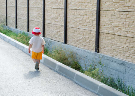 Cute little boy in colourful summer shorts and sunhat walking away alone along a drivewayの写真素材