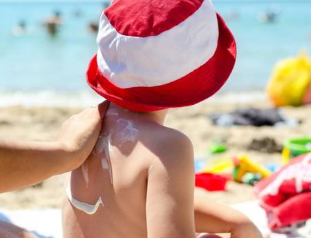 Young boy sitting on the beach during his summer vacation having sunscreen applied to his back by a parent to prevent burning from harmful UV raysの写真素材