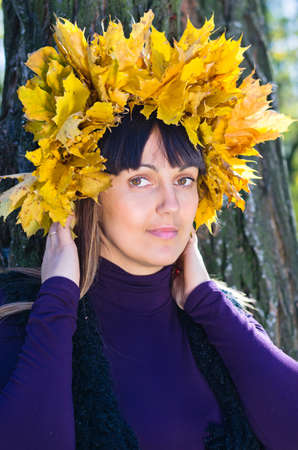 Attractive woman in a hat made from colourful vibrant yellow autumn leaves celebrating the fall seasonの写真素材