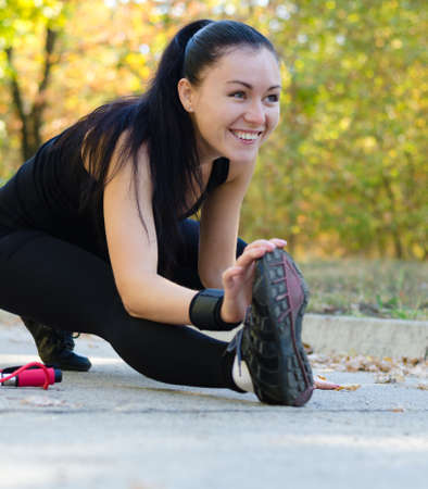 Happy woman exercising in a park bending forwards low on the ground touching her toes as she...