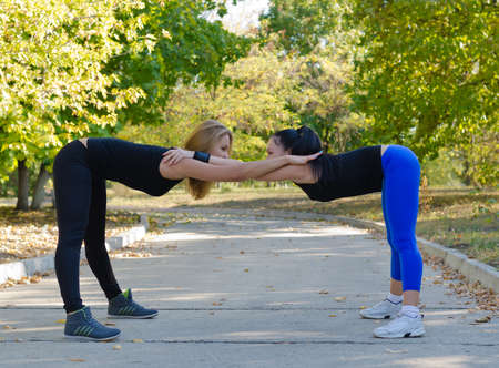 Pair of women working out together doing bending and stretching exercises using each other for mutual supportの写真素材