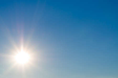 Background image of a bright sun flare in clear blue sky with plenty of copyspaceの写真素材