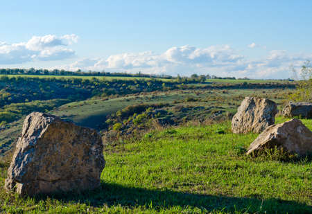 Background image of rocks on green grass in open countryside on a lovely sunny day with blue sky and clouds on the horizonの写真素材