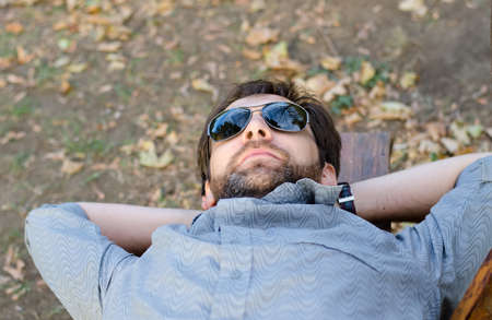 Man with sunglasses lying on bench, enjoys in parkの写真素材